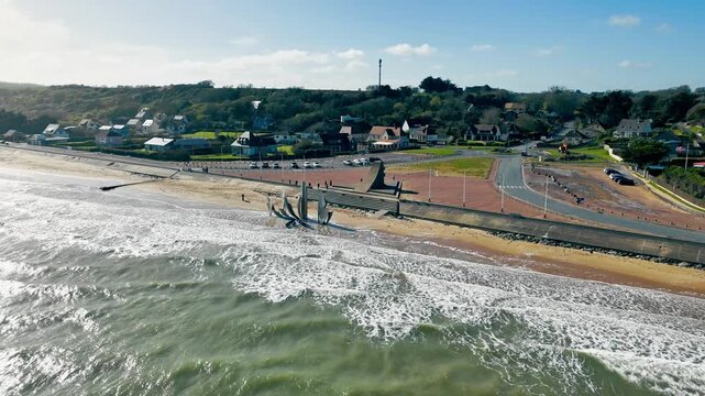 Omaha Beach coastal memorial in Normandy, France, with Les Braves sculpture and breaking waves. Drone view of D-Day remembrance site.