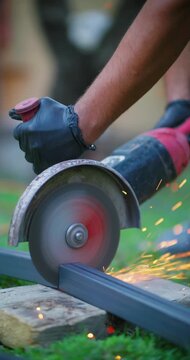 Worker hand cutting square metal tubing with an angle grinder