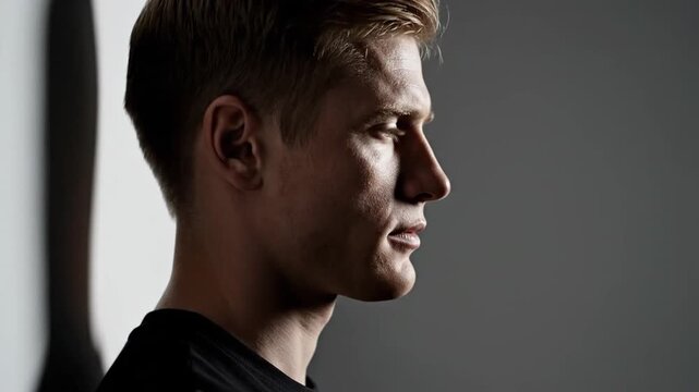 Side profile of a young man with a serious expression, illuminated by dramatic side lighting against a dark background, capturing a contemplative and stoic atmosphere.