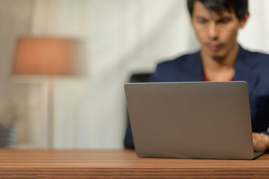 Young man using laptop at desk working or studying indoors with blurred background