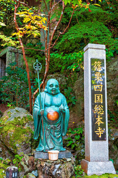 Bronze statue at Nanzoin Temple in Fukuoka shows a figure holding an orb and standing beside a stone marker