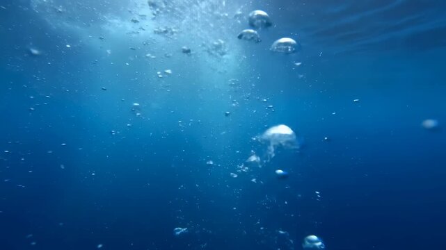 Static shot of air bubbles rising upward through deep blue underwater ocean water