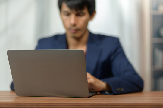 Professional Man Working on Laptop in Office Environment with Bookshelf Background