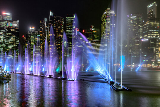Light and water show creates colorful displays in Marina Bay at night in Singapore near tall buildings