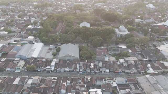 Aerial view captures quiet morning over dense residential neighborhood. Buildings cluster closely, rooftops gleam in soft sunlight. Trees stand tall, framing houses and open spaces. d log m
