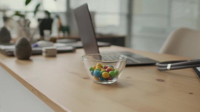 Glass bowl of colorful candies sitting on wooden desk next to stethoscope and laptop in pediatric clinic. Footage is ideal for pediatric healthcare marketing and medical clinic promotions