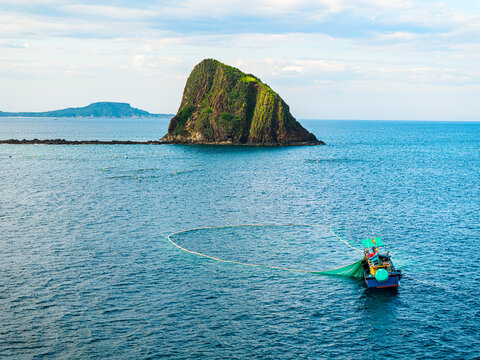 Drone view shows an anchovy fishing boat using nets in the ocean near a rocky island in Vietnam