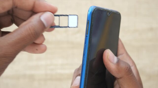 Man inserting SIM card tray into blue smartphone on wooden table