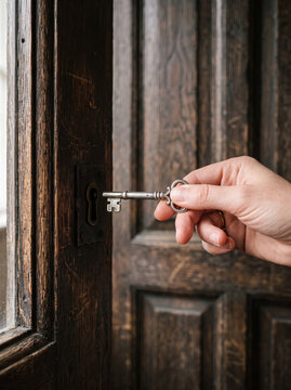 Unlocking dark wooden door with a vintage key