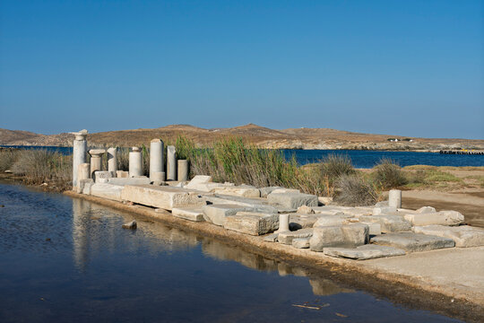 Ruins of ancient columns along the water's edge at Delos archaeological site in Greece