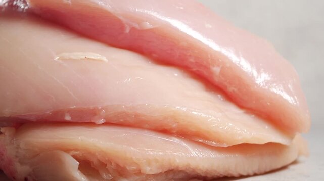 Close up cinematic footage of fresh raw chicken breast fillets stacked on a clean white surface ready for cooking healthy meal preparation