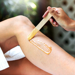 Fototapeta premium Close-up of a person applying wax on their leg with a wooden spatula for hair removal.