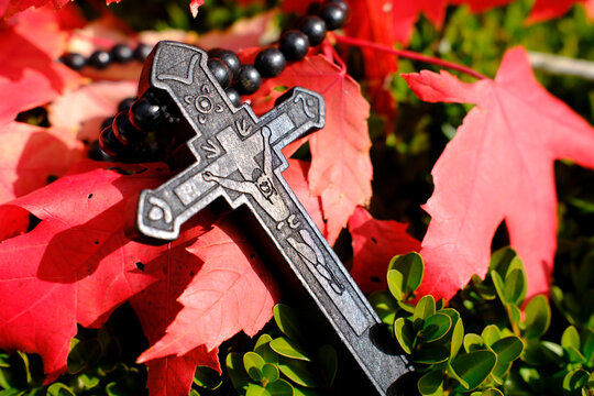 Black ebony rosary with carved crucifix placed on vibrant red autumn leaves for seasonal reflection in France