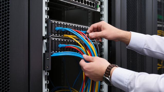 Network administrator managing server cables, Hands connecting ethernet patch cords in rack, Datacenter hardware maintenance process, Server room cable management close-up