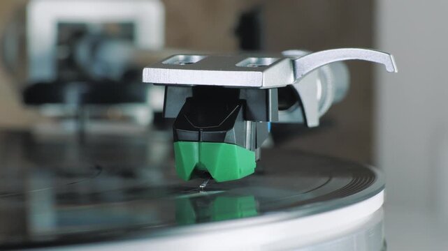 Turntable stylus lowering onto vinyl LP groove, tonearm and cartridge in macro closeup, analog audio playback, hi-fi music equipment, shallow depth of field.