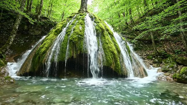 Bigar Waterfall flows over mossy rocks in Romania surrounded by green trees