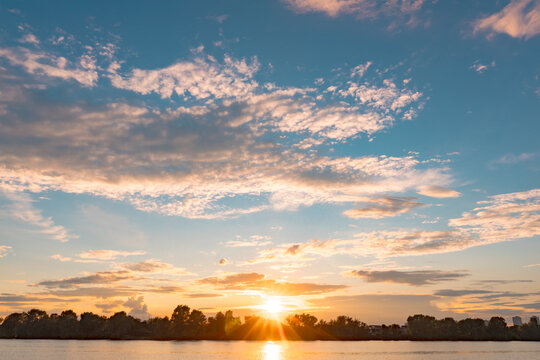 Summer sunset over calm water. Tranquil scenery. Riverbank with trees.