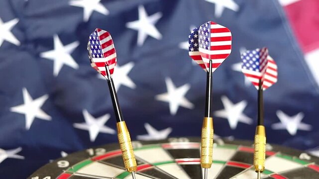 Patriotic darts featuring American flags stuck into a board with a blurred United States flag moving in the background during a bright day