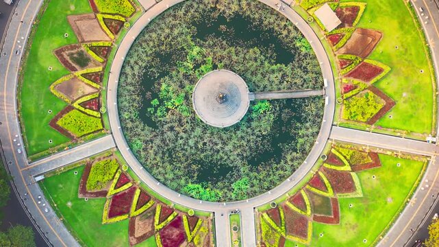 Golden hour bathes historic building and central monument. Circular pond reflects sky and structure. Lush greenery surrounds the scene. Distant trees frame the peaceful vista