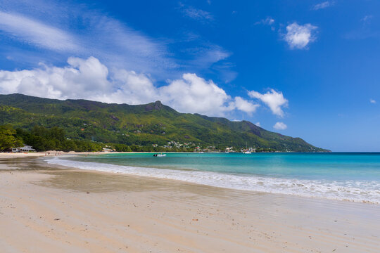 Landscape of Beau Vallon beach on a sunny summer day. Wet sandy shore is under bright blue sky with white clouds, Mahe island, Seychelles