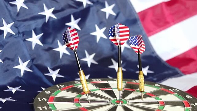 Three metal darts featuring American flag designs stand firmly in a circular board while the Stars and Stripes wave in the background to show patriotism during a sunny afternoon event