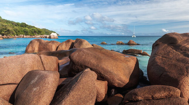Coastal rocks and shore water of Anse Lazio beach on a sunny day, panoramic landscape photography of Praslin, Seychelles