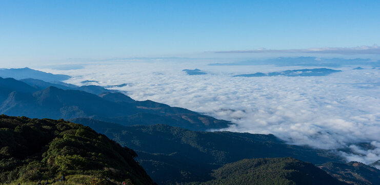 Mountain landscape above a vast sea of clouds under clear blue sky and morning light.