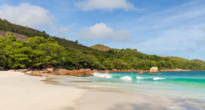 Anse Lazio beach scene with turquoise sea, powder-white sand and weathered granite rocks framed by leafy green foliage under a bright blue sky, evoking relaxation, escape and coastal serenity