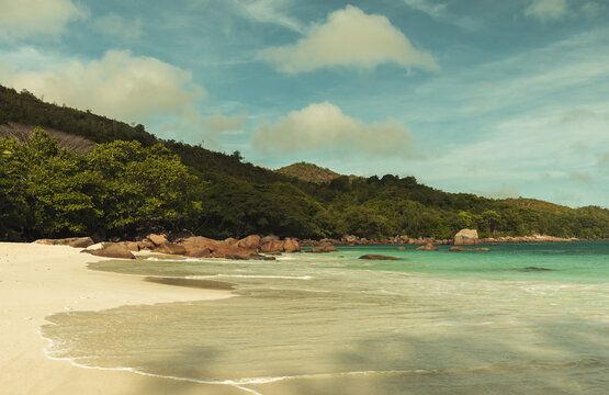 Anse Lazio beach view with wet rocks and shore water on a sunny summer day. Coastal landscape of Praslin island, Seychelles. Vintage tonal correction filter effect