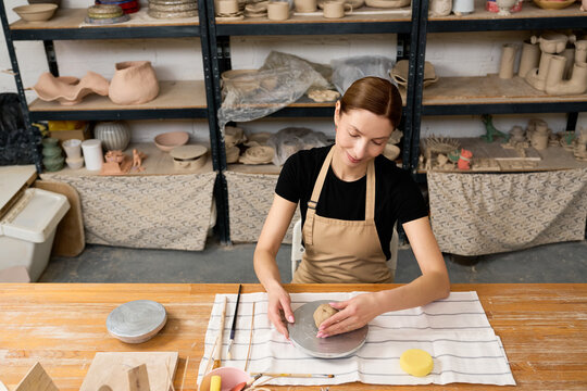 Beautiful woman potter shaping clay in her cozy ceramic workshop