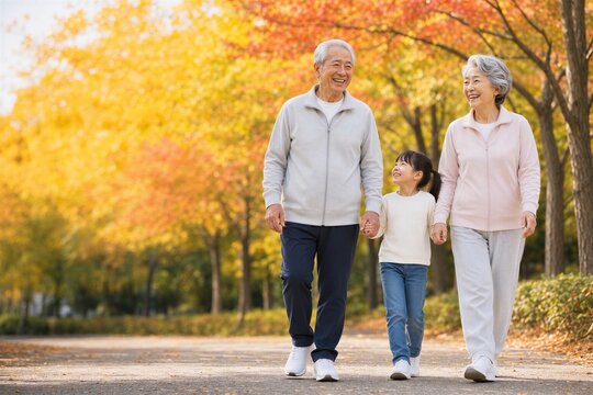 紅葉の公園を孫と手をつないで歩く日本人祖父母