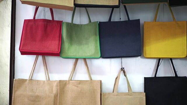 Colorful jute bags in various colors red, green, blue, yellow, and black hanging on a white wall in a shop or market, eco-friendly tote bags display
