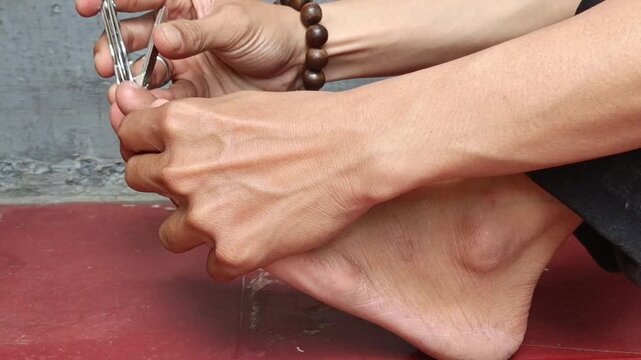 Someone trimming their toenails with a nail clipper at home. A daily hygiene and self-care routine in a clean room.