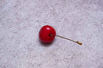 Single Fresh Cherry on Textured Leather. A minimalist close-up shot of red cherry with a stem. Perfect for food, culinary, or still-life design concepts. © ismailgazel