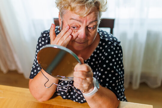 Mature older female holding small mirror checking under eye skin.
