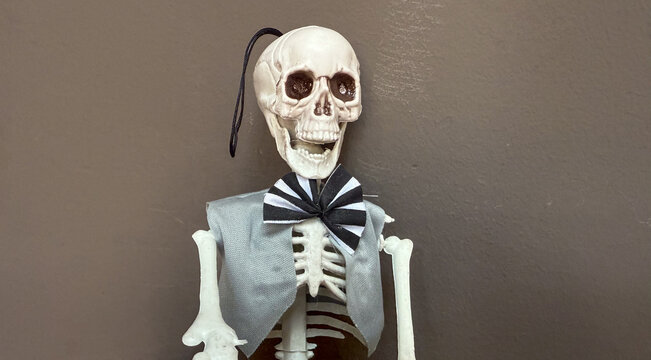 grinning skeleton with bow tie and vest, dark wall, copyspace, concept of halloween, party