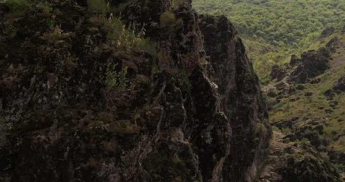A drone flies around a young athletic female climber hanging on one arm on a belay on a steep cliff