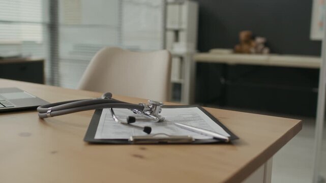 Stethoscope and clipboard resting on desk in empty pediatric office with teddy bears in background. Video useful for healthcare marketing, medical insurance ads, or pediatric clinic promotion