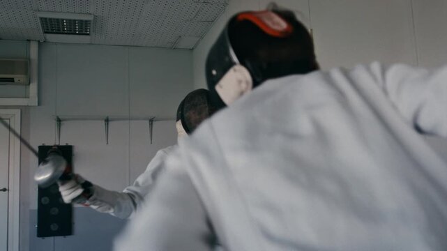 Fencing sport. Sportsmen fencing training. Two swordsmen are doing sword moves. Fencer players in gym, indoor sports club. Two athletes practice epee, uniforms and masks. Olympic combat sport.