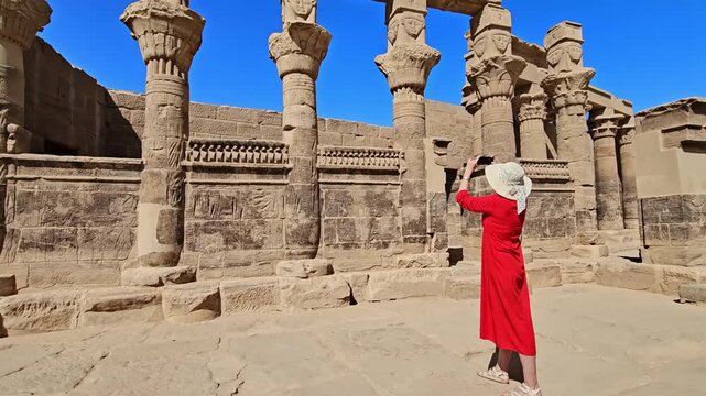 A woman in a red dress exploring the ruins of the Philae Temple, Aswan, Egypt.