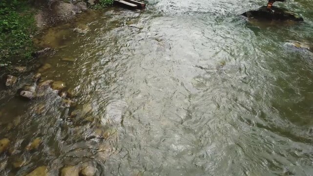Mountain river with narrow wooden footbridge, aerial view