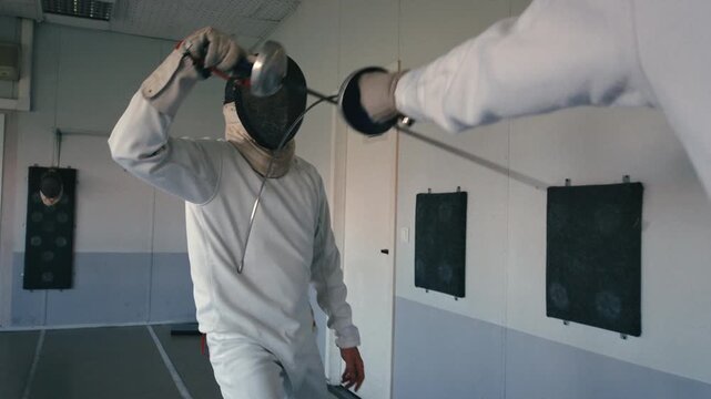 Fencing sport. Sportsmen fencing training. Two swordsmen are doing sword moves. Fencer players in gym, indoor sports club. Two athletes practice epee, uniforms and masks. Olympic combat sport.