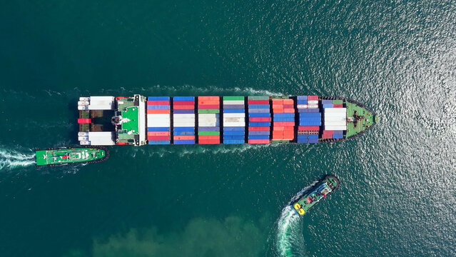 Large container ship navigates through dark ocean waters with escort tugboats assisting its passage to Port, delivering vital cargo amidst challenging maritime conditions.