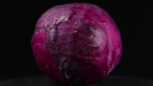 Close-up of a whole red cabbage head texture slowly rotating on a black background.