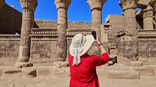 A woman in a red dress exploring the ruins of the Philae Temple, Aswan, Egypt.