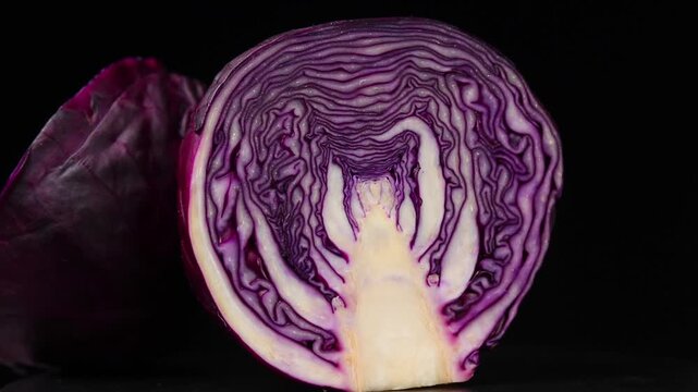 Halved red cabbage head showing texture and pattern, slowly rotating on a black background.