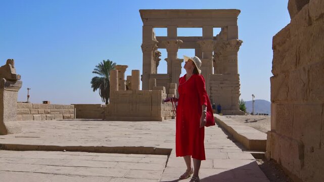 A woman in a red dress exploring the ruins of the Philae Temple, Aswan, Egypt.