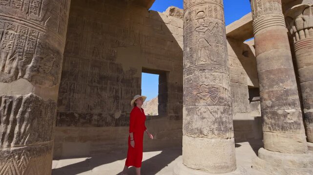 A woman in a red dress exploring the ruins of the Philae Temple, Aswan, Egypt.