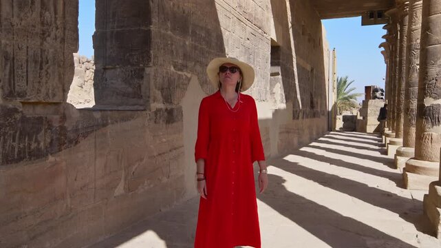 A woman in a red dress exploring the ruins of the Philae Temple, Aswan, Egypt.