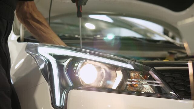 The technician inspects and fine-tunes the headlights of the vehicle's lighting system. The process of adjusting the headlights using a screwdriver at a repair shop.